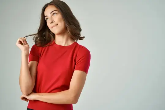 Задумчивая брюнетка в красной футболке накручивает прядь на палец