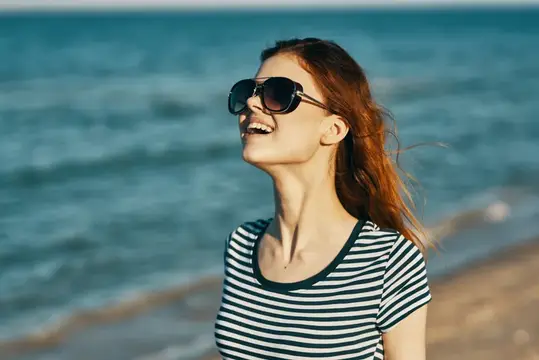 Весёлая женщина в футболке и очках отдыхает на морском берегу в горах