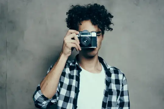 Кудрявый парень в клетчатой рубашке фотографирует на плёночный фотоаппарат