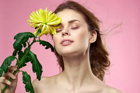 Молодая женщина с закрытыми глазами и жёлтой хризантемой на розовом фоне