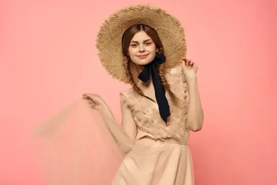 Модная женщина в платье и шляпе с черной лентой на розовом фоне, обрезанный вид, модель демонстрирует эмоции и веселье