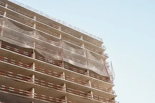 Строящееся высотное здание с защитной сеткой на фоне ясного неба
