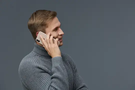 Улыбающийся мужчина в сером свитере говорит по телефону