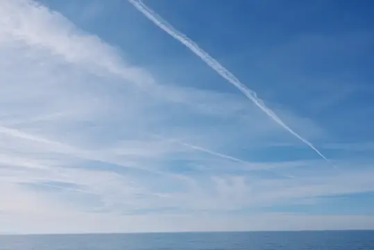 Белый след самолёта на фоне голубого неба над морем