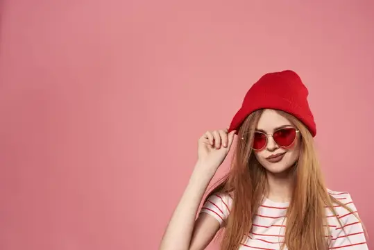 Молодая девушка в красной шапке и очках на розовом фоне