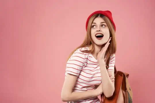 Модная женщина в красной шляпе, с рюкзаком в руках, позирует