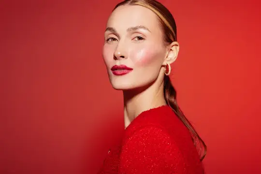 Светловолосая женщина с ярким макияжем на красном фоне