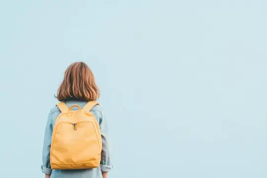 Маленькая девочка с жёлтым рюкзаком смотрит на бледно-голубую стену, вызывая чувства любопытства и приключения
