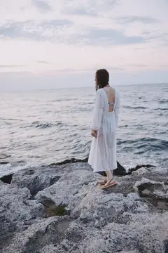 Девушка в белом платье стоит на скалах у моря