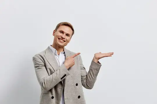 Улыбающийся мужчина в пиджаке показывает рукой в сторону на сером фоне