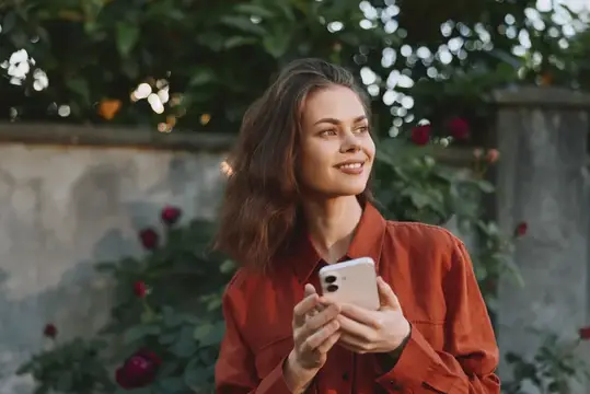 Улыбающаяся девушка с телефоном в руках на фоне роз