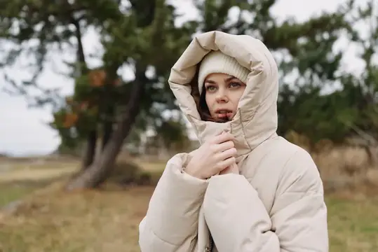 Сцена на открытом воздухе: фигура в капюшоне и теплой куртке стоит рядом с открытым полем и деревьями