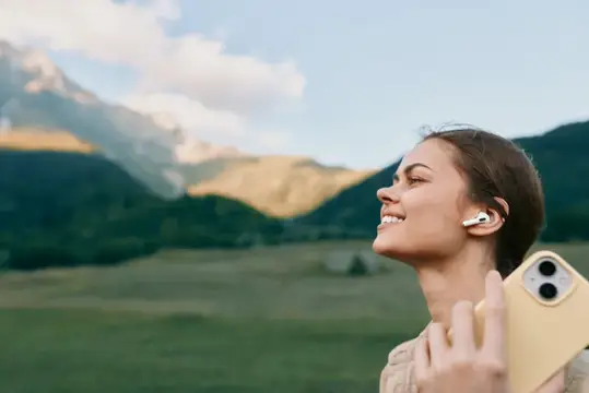 Улыбающаяся девушка в наушниках на фоне гор