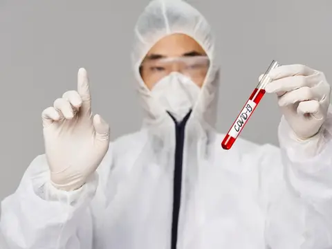 Медик в защитном костюме держит пробирку с анализом на COVID-19