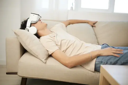 Молодой человек в VR-очках лежит на диване с закрытыми глазами