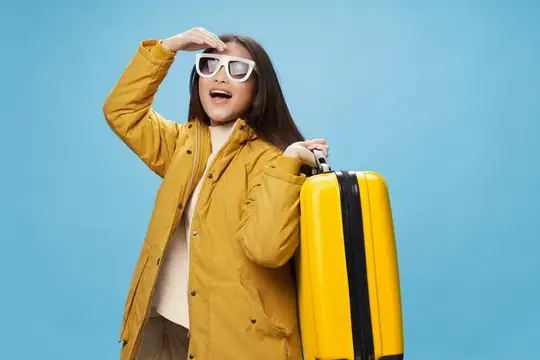 Удивлённая девушка в жёлтом плаще с чемоданом смотрит вдаль