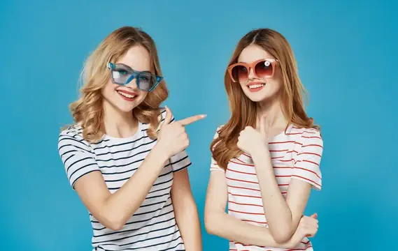 Две смеющиеся девушки в солнцезащитных очках на синем фоне
