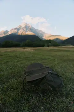 Тёмный рюкзак лежит на траве на фоне гор