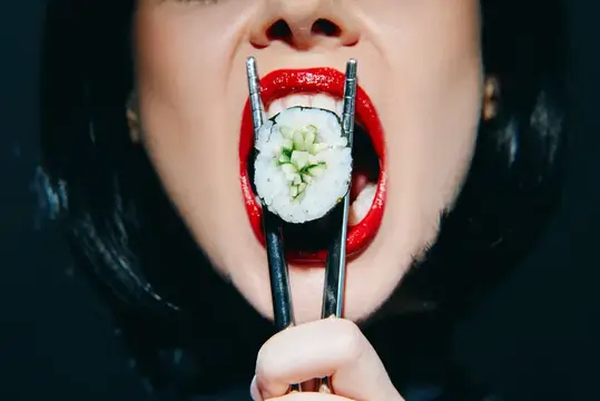 Крупный план женщины с ярко-красными губами, держащей суши палочками в драматичной позе, подчеркивающий современную культуру еды и яркие цвета в художественном стиле