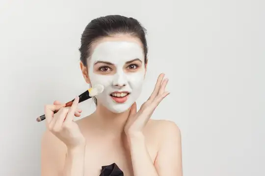 Молодая женщина наносит белую глиняную маску кистью на лицо