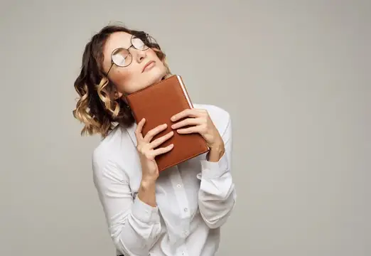Девушка в очках мечтательно прижимает к себе коричневую книгу