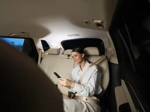 Женщина сидит на заднем сиденье автомобиля, сосредоточенно глядя в мобильный телефон, что отражает момент современной связи и концентрации