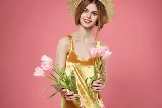 Улыбчивая девушка в соломенной шляпе с букетом розовых тюльпанов на розовом фоне