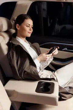 Ухоженная женщина в светлом салоне автомобиля смотрит в смартфон