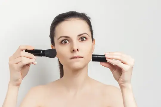Молодая женщина с двумя кистями для макияжа у лица на сером фоне