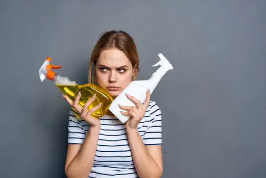 Уставшая молодая женщина с двумя бутылками чистящего средства