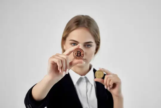 Девушка в деловом костюме держит биткоин перед лицом