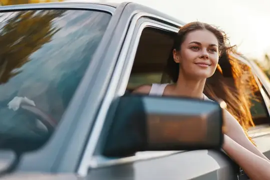 Улыбающаяся девушка высунулась из окна автомобиля на закате