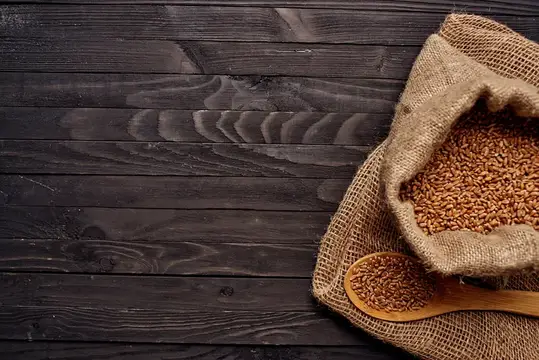Мешок с пшеничным зерном и деревянная ложка на тёмном столе