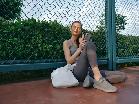 Спортивная девушка отдыхает с телефоном у сетки на корте