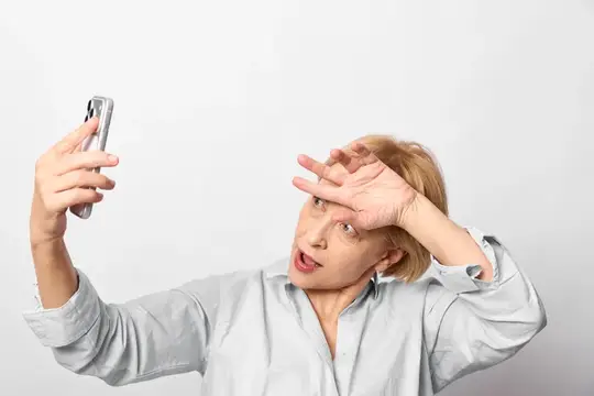 Блондинка в рубашке делает селфи с удивлённым лицом на белом фоне