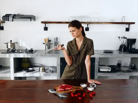 Молодая женщина с ножом готовит мясо на кухне