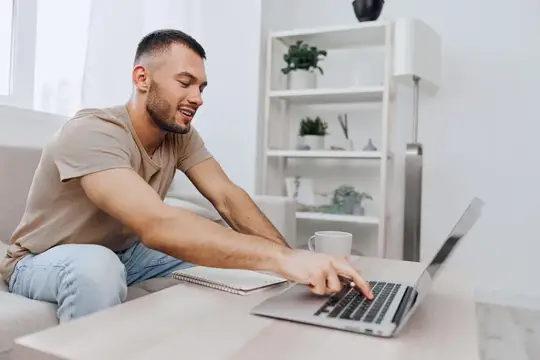 Улыбающийся мужчина сосредоточенно работает на ноутбуке в стильном и светлом домашнем офисе, подчёркивая суть трендов удалённой работы в 2025 году, делая акцент на продуктивности и комфорте