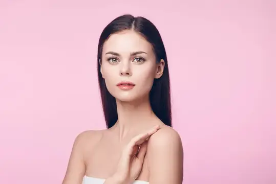 Молодая темноволосая женщина с ухоженной кожей на розовом фоне