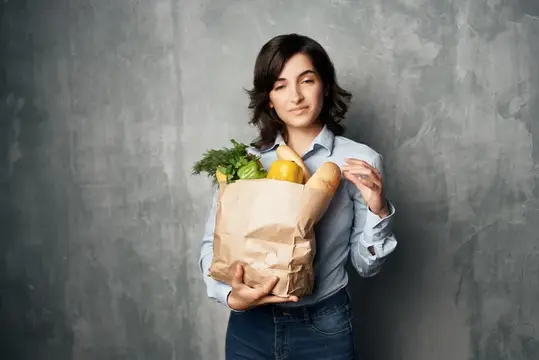 Молодая женщина с бумажным пакетом продуктов на сером фоне