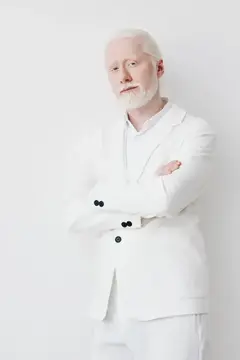 Альбинос в белом костюме со скрещёнными руками на светлом фоне
