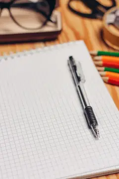 На рабочем столе лежат блокноты, фломастеры, канцелярские принадлежности и очки в футляре