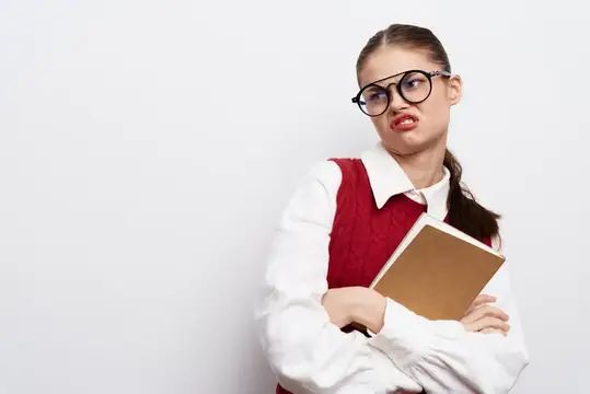 Недовольная школьница в очках с книгой кривит лицо на белом фоне