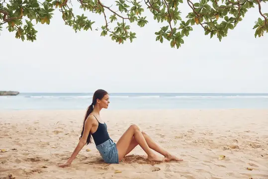 Молодая женщина отдыхает на песчаном пляже под кроной дерева
