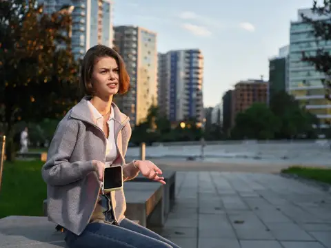 Молодая женщина с телефоном сидит на набережной в городе