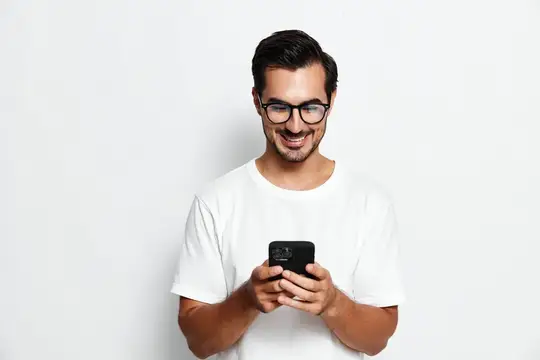 Улыбающийся мужчина в очках смотрит в смартфон на белом фоне
