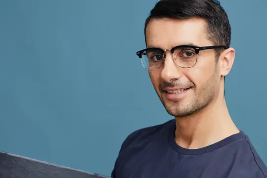 Улыбающийся темноволосый мужчина в очках на синем фоне