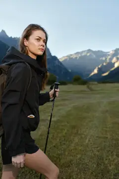 Молодая женщина с треккинговой палкой на фоне горных вершин