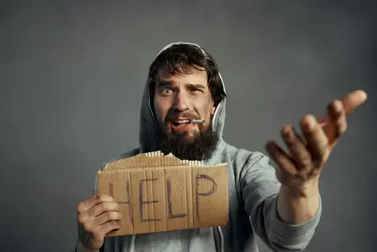 Бородатый мужчина в капюшоне с табличкой HELP просит о помощи