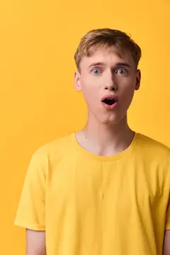 Удивленный светловолосый парень с открытым ртом на желтом фоне
