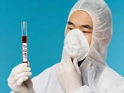 Азиатский лаборант в защитном костюме держит пробирку с анализом на COVID-19